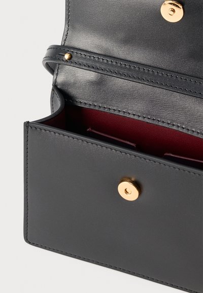 Μαύρη δερμάτινη τσάντα με δομημένο σχήμα, ανοιχτό καπάκι, χρυσό κουμπί και βαθιά κόκκινη εσωτερική επένδυση ορατή στο εσωτερικό.