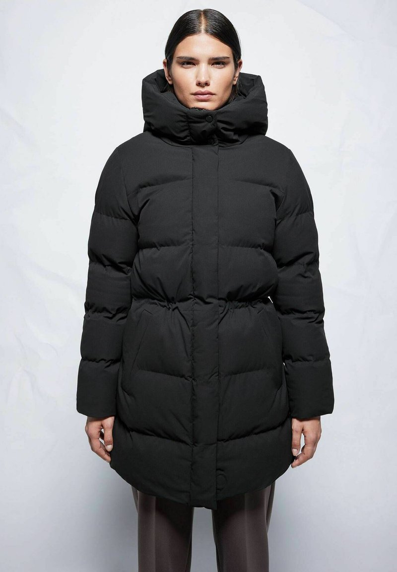 Schwarze Pufferjacke mit hohem Kragen, Knopfverschluss und elastischem Bund. Die Jacke hat ein gesteppter Design und lange, voluminöse Ärmel.