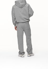 Grå hoodie och joggingbyxor i mjukt material, med en avslappnad passform, unik sömdetalj och en liten texttryck på baksidan.