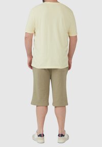 Jasnożółta, krótkosleevena koszulka w zestawie z oliwkowozielonymi szortami do kolan. Luźny materiał, wygodny krój oraz białe trampki z granatowymi akcentami.