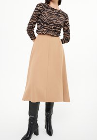Long beige skirt with a smooth texture and A-line shape, paired with a black top featuring wavy orange patterns. Black knee-high heeled boots.