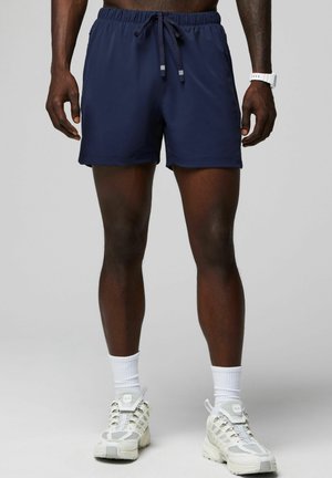 Shorts de bain bleu marine avec une taille élastique et un cordon de serrage. Tissu lisse, longueur au-dessus du genou, sans poches visibles ni motifs.