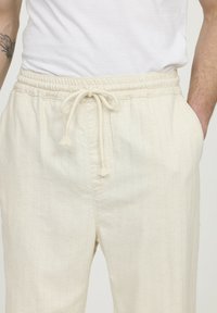 Lichtbeige broek van textiel met een gestructureerde stof, met een tailleband met trekkoord en verticale strepen. De zijzakken zijn zichtbaar.
