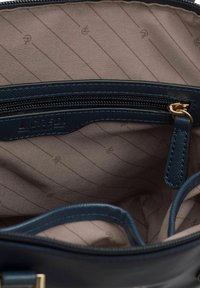 Interno di una borsa a mano in pelle blu navy con tasca con zip, foderato in beige con sottili righe e una superficie liscia. Accessori in tono oro.