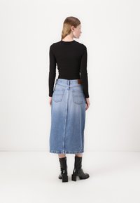 Svart langermet topp parret med en lys blå denim maxiskjørt med to baklommer og frynsete kant. Svart helhælte ankelstøvler inkludert.