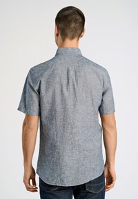 Camicia a maniche corte con bottoni in tessuto azzurro chiaro con finitura testurizzata. Presenta un colletto classico e una piega sul retro per facilitare i movimenti.