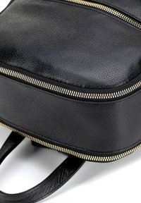 Sac à dos en cuir noir avec deux compartiments zippés, surface texturée et quincaillerie en ton doré. Équipé de deux poignées robustes pour le transport.