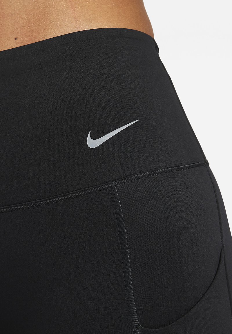 Zwarte sportleggings gemaakt van een gladde stof, met een klein zilveren Nike-logo op de taille en een zijzak ontwerp.