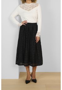 Witte blouse met lange mouwen en kantdetails op het lijfje en de manchetten, gecombineerd met een zwarte midi rok met bloemenpatronen en plooien.