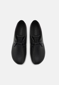 Paire de chaussures en cuir noir à lacets avec bouts arrondis, vues de dessus sur fond blanc uni.