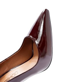 Zapato de charol burdeos con punta afilada, lados recortados y un interior suave. Presenta un tacón delgado y elegante, y un diseño minimalista.