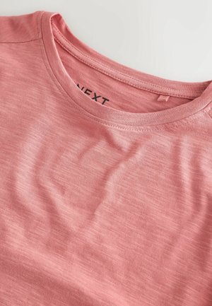 Světle růžové tričko vyrobené z měkké tkaniny, s kulatým výstřihem a jemnou texturou. Na vnitřní straně štítek s nápisem "NEXT".