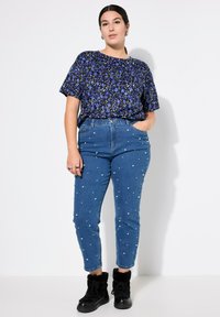 Top blu floral a maniche corte con vestibilità ampia, abbinato a jeans in denim a vita alta decorati con perle sintetiche bianche e stivaletti neri.