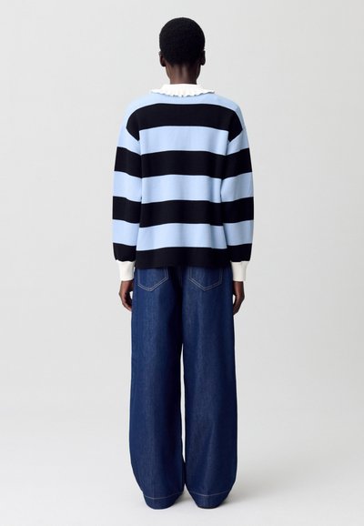 Suéter a rayas en azul claro y negro con un cuello blanco con volantes, combinado con pantalones de mezclilla oscuros y holgados.