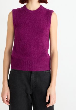 Ärmelloses, flauschiges, lila Strickoberteil, getragen zu hoch taillierten schwarzen Jeans an einer Person, die vor einem weißen Hintergrund steht.