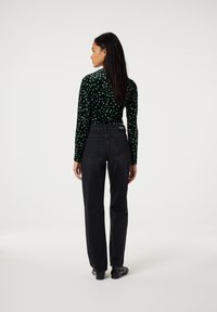 Zwarte hoge taille jeans met rechte pijpen, gecombineerd met een langmouwige top met een patroon dat groene en blauwe abstracte vormen toont.