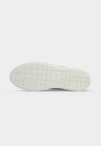 Semelle en caoutchouc blanc de basket avec motifs de bande de roulement rectangulaires et striés sur un fond clair uni.