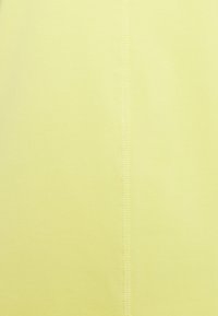 Helles gelbes Gewebe mit einer glatten Textur und einer zentralen Naht. Die Stiche sind sichtbar und fügen dem Gesamtdesign ein subtile Detail hinzu.