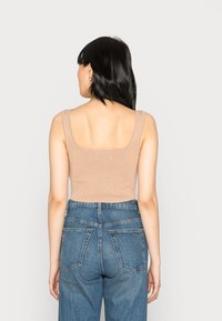 Top cropped em malha bege com decote quadrado e alças largas, combinado com jeans de denim azul de cintura alta com bolsos traseiros.