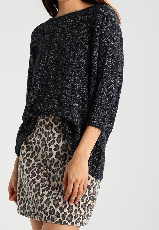 Maglione nero lavorato a maglia con scollatura ampia e maniche a tre quarti, abbinato a una gonna beige con stampa leopardata che mostra la sua trama e il suo motivo.
