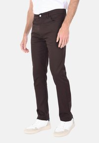 Pantaloni slim-fit marroni realizzati in un morbido misto cotone. Presentano una chiusura con bottone frontale e tasche laterali, abbinati a sneakers bianche.