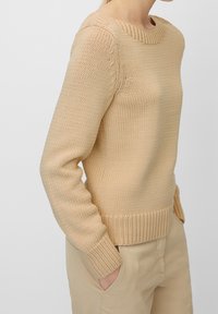 Pull beige en maille avec un col rond, des poignets et un ourlet côtelés. Tissu légèrement texturé et coupe ajustée avec manches montées.