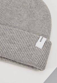 Grey knit beanie hat with a ribbed texture, featuring a folded cuff and a small white tag with black text attached.
