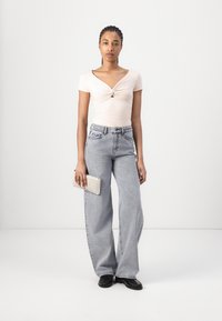 Top rosa chiaro a maniche corte con dettaglio davanti torcigliato, abbinato a jeans grigi chiari a gamba larga e una pochette grigia chiara strutturata. Mocassini neri.
