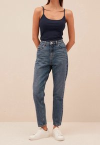 Jeans blu a vita alta con gamba affusolata, realizzati in denim, abbinati a un top aderente blu navy e sneakers bianche.