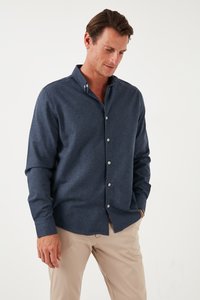 Camicia button-up blu navy con una consistenza morbida e un design aderente, dotata di colletto e maniche lunghe, abbinata a pantaloni beige.