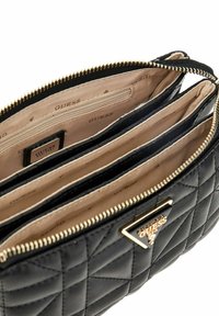 Portefeuille matelassé noir avec fermeture éclair et détails en ton or. Plusieurs compartiments doublés de tissu beige, présentant le logo Guess.