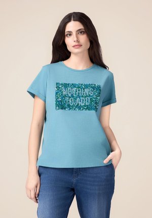 T-shirt vert d'eau à manches courtes en coton, présentant un rectangle pailleté bleu et vert avec le texte "RIEN À AJOUTER."