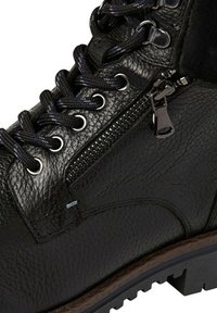 Bottine en cuir noir avec finition texturée, dotée de lacets ronds, d'une fermeture éclair sur le côté et d'une semelle en caoutchouc robuste avec un contour en brun contrasté.