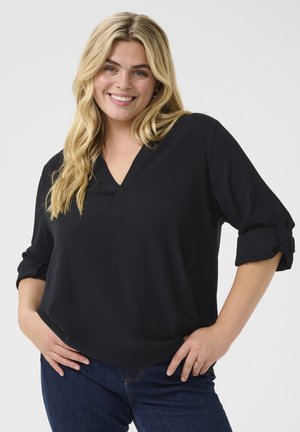 Schwarze Waffelstrick-Bluse mit V-Ausschnitt, 3/4 gerollten Ärmeln und lockerer Passform. Kombiniert mit dunkelblauen Jeans.