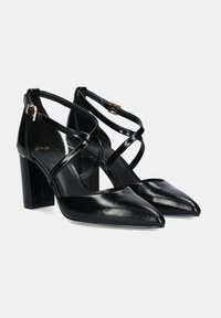 Tacones altos de cuero negro con punta afilada, que presentan correas cruzadas y un tacón cuadrado. Textura suave y un brillo sutil.