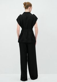 Haut noir ceinturé avec des manches courtes, associé à un pantalon noir à jambes larges. Tissu lisse avec une coupe ajustée et un détail plissé au dos.