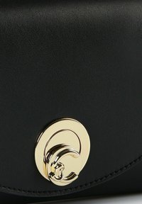 Borsa a tracolla in pelle nera con una chiusura circolare in oro ben visibile e finitura testurizzata, con bordo curvo e dettagli di cucitura raffinati.