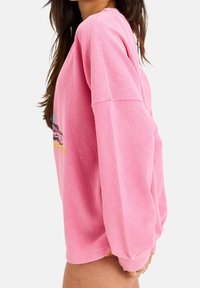 Różowa, oversize'owa bluza z długim rękawem o fakturze wafla, z kolorowym, graficznym nadrukiem z przodu. Luźny fason z opuszczonymi ramionami.