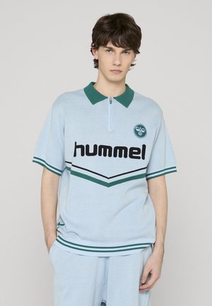 Hellblaues Poloshirt mit einem Reißverschluss am Ausschnitt, grünem Kragen und schwarzem "hummel"-Logo. Verfügt über gestreifte Akzente in Grün und Schwarz.