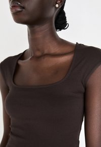Bruine fitted top met een vierkante halslijn en korte mouwen, gemaakt van gladde stof, die de natuurlijke schouder- en sleutelbeencontouren accentueert.