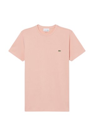 Camiseta de algodón de color rosa claro con mangas cortas, escote redondo y un pequeño logo verde de Lacoste en el lado izquierdo del pecho. Diseño liso, textura suave.