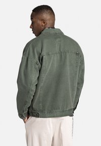 Grøn denimjakke med en afslappet pasform, der har en klassisk krave, sidelommer og knaplukninger. Stoffet har en blød, slidt tekstur.