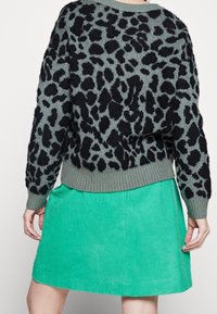 Stickad tröja i grönt med ett svart leopardmönster, med en ribbad nederkant och breda ärmar. Matchad med en enfärgad grön manchesterkjol.