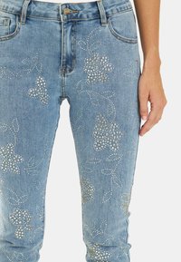 Jeans in denim azzurro chiaro con un motivo floreale in strass argentati, dalla forma aderente e un leggero effetto sbiadito nel tessuto.