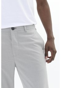 Pantaloni de culoare gri cu un model, având un croi drept, buzunare laterale și închidere cu nasture, asortați cu o cămașă albă simplă.