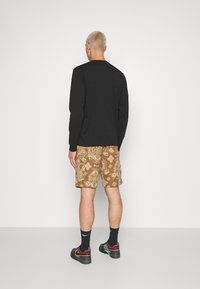 Cămașă neagră cu mânecă lungă, pantaloni șort cu model maro și pantofi negri cu accente colorate. Material neted, croială lejeră și designuri detaliate.