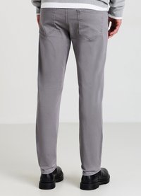 Graue Baumwollhosen mit Slim-Fit, ausgestattet mit zwei Gesäßtaschen und verstärkten Nähten; kombiniert mit schwarzen strukturierten Schuhen.