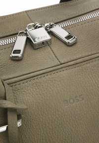 Olive green leather bag featuring silver hardware, double zipper, and embossed "BOSS" logo. Textured surface with clean stitching details.