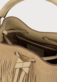 Τσάντα χειρός από μπεζ σουέτ με δερμάτινες λεπτομέρειες, εσωτερική επένδυση και χρυσά μεταλλικά στοιχεία. Διαθέτει διακόσμηση φιόγκου και σχέδιο με κρόσσια στο εξωτερικό μέρος.