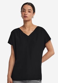 Top nero a maniche corte con scollatura a V. Realizzato in un tessuto liscio, ha una vestibilità rilassata e un design minimalista senza motivi o grafiche.